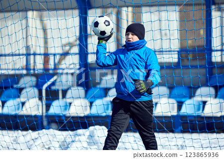 Goalkeeper's Catch. Boy in blue gear secures soccer ball in firm grip, ensuring team's defense remains solid during training on cold day. Goalkeeper's Catch. Boy in blue gear secures soccer ball in firm grip, ensuring team's defense remains solid during training on cold day. 123865936