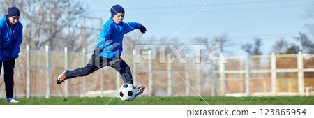 Perfecting goal shots. Young athlete executing powerful kick towards goal on green outdoor field, focusing on technique and accuracy. 123865954