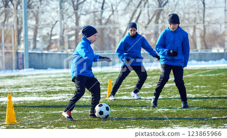 Young footballers maneuvering between cones, refining dribbling skills under mentor's guidance. Teamwork and determination. 123865966