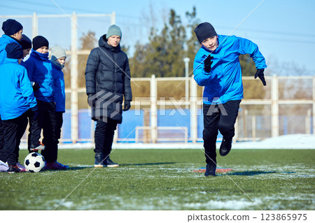 Building Coordination. Junior soccer player training dribbling speed and agility in snowy outdoor stadium. Motivation and progress. 123865975