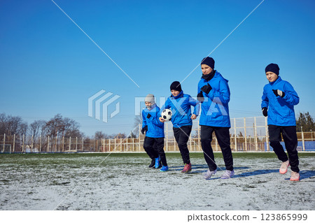 Strength in Unity. Young football players in matching uniforms running on frozen pitch, pushing through winter conditions. 123865999