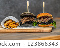 Burger with pulled meat in a dark and light bun with fresh vegetables and french fries on a wooden board 123866343