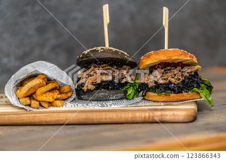 Burger with pulled meat in a dark and light bun with fresh vegetables and french fries on a wooden board 123866343