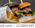 Burger with pulled meat in a dark and light bun with fresh vegetables and french fries on a wooden board 123866345