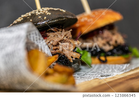 Burger with pulled meat in a dark and light bun with fresh vegetables and french fries on a wooden board 123866345