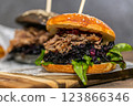 Burger with pulled meat in a dark and light bun with fresh vegetables and french fries on a wooden board 123866346