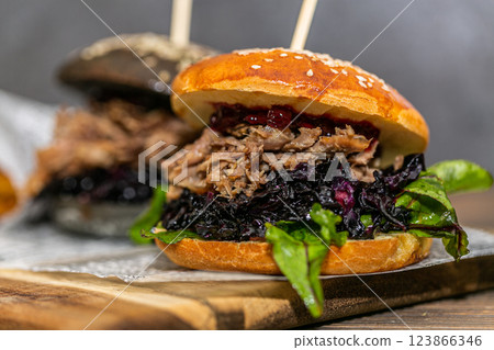 Burger with pulled meat in a dark and light bun with fresh vegetables and french fries on a wooden board Burger with pulled meat in a dark and light bun with fresh vegetables and french fries on a wooden board 123866346