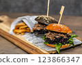 Burger with pulled meat in a dark and light bun with fresh vegetables and french fries on a wooden board 123866347