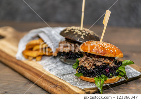 Burger with pulled meat in a dark and light bun with fresh vegetables and french fries on a wooden board 123866347