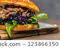 Burger with pulled meat in a dark and light bun with fresh vegetables and french fries on a wooden board 123866350