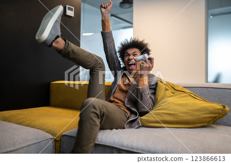 Curly-haired young man looking excited while playing video games during the break at work Curly-haired young man looking excited while playing video games during the break at work 123866613