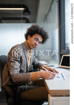 Dark-skinned businessman working on the project and looking serious Dark-skinned businessman working on the project and looking serious 123866670