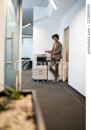 Curly-haired young businessman standing near xerox and making documents copies 123866684
