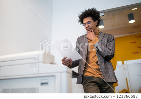 Curly-haired young businessman standing near xerox and making documents copies Curly-haired young businessman standing near xerox and making documents copies 123866688
