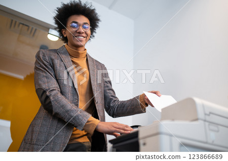 Curly-haired young businessman standing near xerox and making documents copies Curly-haired young businessman standing near xerox and making documents copies 123866689