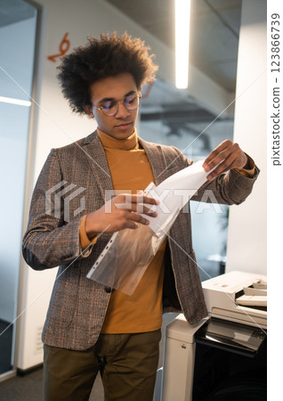 Young man putting the documents in the file and looking involved Young man putting the documents in the file and looking involved 123866739