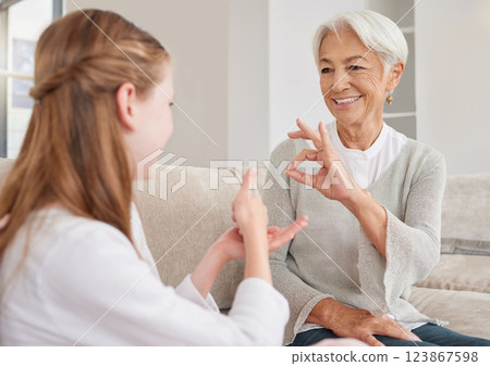 Senior woman, sign language and deaf girl communication, talking or conversation in home. Support, care and retired old female speaking to child with hearing disability in asl language hand gestures. 123867598