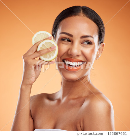 Face, skincare and woman with lemon for health, wellness and vitality on orange studio background. Model, smile and female from Canada with citrus fruit for healthy vitamin c, minerals or nutrition. 123867661