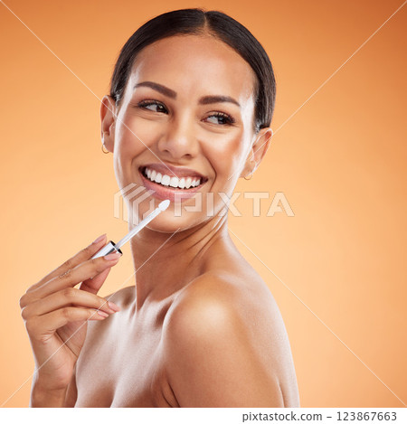 Face, beauty makeup and woman with lip gloss, product or cosmetics on orange studio background. Lip care, smile and model from Canada with lipstick, lips and mouth treatment for fresh glossy finish. 123867663
