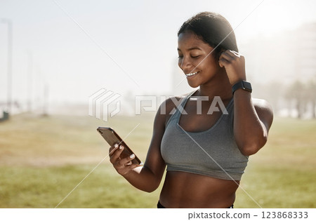 Black woman, music earphones or phone for fitness podcast, exercise motivation or training radio on sports grass field. Smile, happy and mobile technology for athlete or workout health data on 5g app 123868333