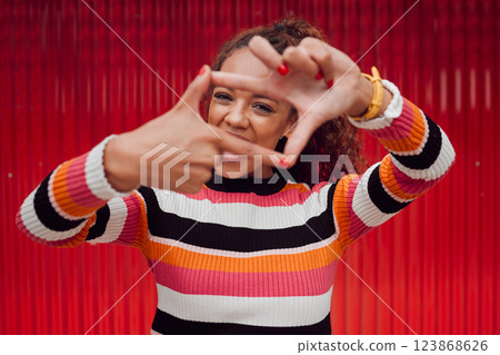 Happy, black woman and finger frame over eyes for funny face expression on red background. Fashion, comic and positive perspective with female from South Africa with hand gesture feeling playful 123868626