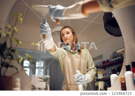 Small business, clean salon and woman to prepare for hygiene, mirror cleaning or with spray bottle. Female entrepreneur, hairdresser or wiping surface or girl getting shop ready or after work hours 123868725