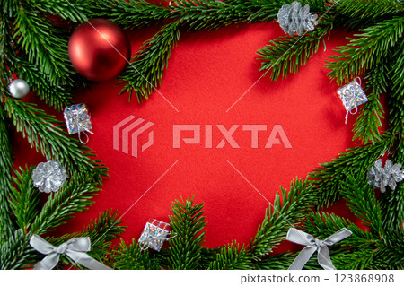 Red bright Christmas background. Winter frame of green branch, silver cones and gifts for decor on the textured fabric background. Copy space. Top view. Red bright Christmas background. Winter frame of green branch, silver cones and gifts for decor on the textured fabric background. Copy space. Top view. 123868908