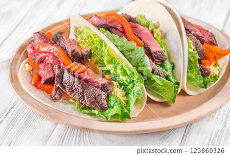 Three carne asada tacos filled with steak, grilled peppers, lettuce, and cheese 123869326