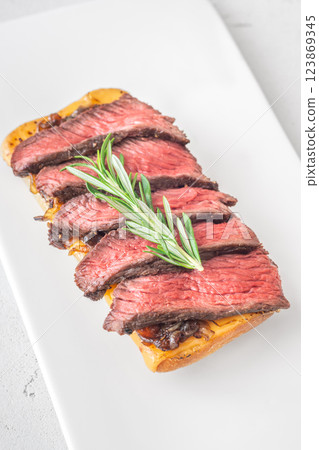Grilled ciabatta sandwich with melted cheese, juicy steak, caramelized onions, and rosemary 123869345