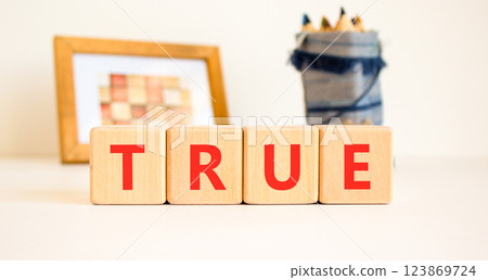 True symbol. Concept word True on beautiful wooden blocks. Beautiful picture frame and colored pencils. Beautiful white table white background. Business, lifestyle, support true concept. Copy space. 123869724