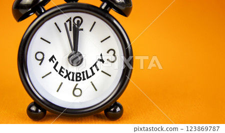 Flexibility symbol. Concept word Flexibility on beautiful orange paper. Beautiful orange paper background. Black alarm clock. Business flexibility concept. Copy space. Flexibility symbol. Concept word Flexibility on beautiful orange paper. Beautiful orange paper background. Black alarm clock. Business flexibility concept. Copy space. 123869787