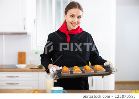 Proffesional woman in chef uniform holding sheet pan with just baked cupcakes 123870555