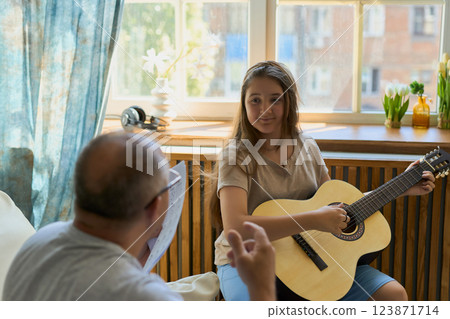 Grandpa teaching his granddaughter to play guitar on sofa at home Grandpa teaching his granddaughter to play guitar on sofa at home 123871714