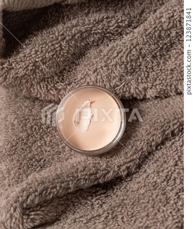 Opened lip balm jar on brown bath towel top view. Herbal cosmetic product for daily lipcare Opened lip balm jar on brown bath towel top view. Herbal cosmetic product for daily lipcare 123871841