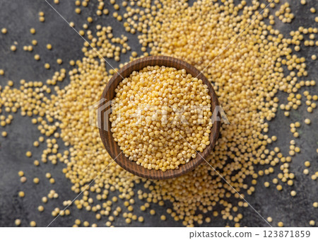 Wooden bowl of raw uncooked yellow pearl hulled millet grain on gray table top view. Ancient food Wooden bowl of raw uncooked yellow pearl hulled millet grain on gray table top view. Ancient food 123871859