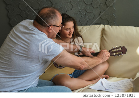 Grandpa teaching his granddaughter to play guitar on sofa at home Grandpa teaching his granddaughter to play guitar on sofa at home 123871925