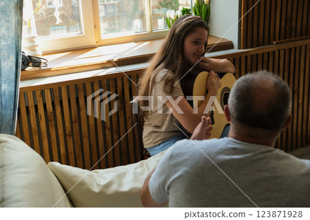 Grandpa teaching his granddaughter to play guitar on sofa at home 123871928