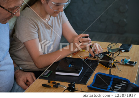 Grandfather and granddaughter work together on an electronics project 123871937
