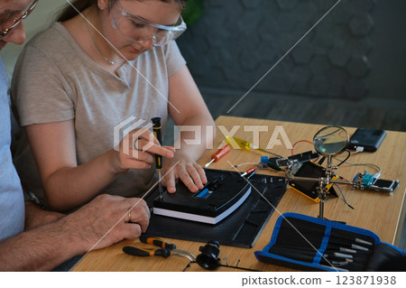 Grandfather and granddaughter work together on an electronics project 123871938