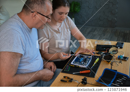 Grandfather and granddaughter work together on an electronics project Grandfather and granddaughter work together on an electronics project 123871946