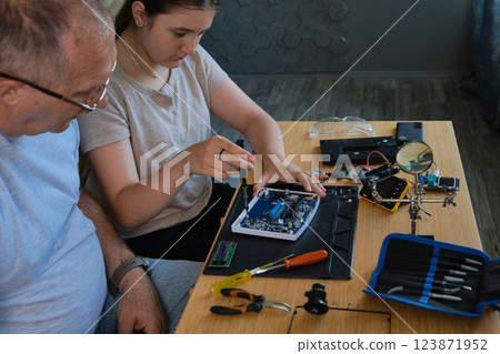 Grandfather and granddaughter work together on an electronics project Grandfather and granddaughter work together on an electronics project 123871952