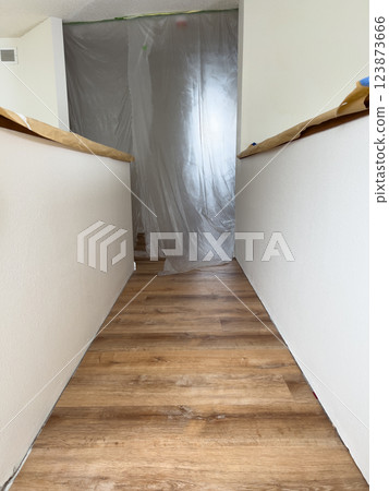 A freshly renovated upstairs hallway featuring new wood-look flooring. The walls are painted white, and protective plastic sheeting covers an entryway, indicating ongoing construction or remodeling 123873666