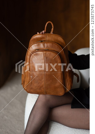 A girl in a warm sweater, a black short skirt, nylon tights, and black shoes is posing with a brown backpack. A girl in a warm sweater, a black short skirt, nylon tights, and black shoes is posing with a brown backpack. 123873745