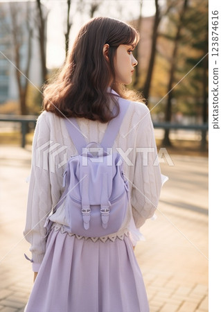A student with a violet lavender backpack in school uniform, walking on a campus outdoors, seen from behind. A high school or university teenager girl. Casual teen outfit fashion. Light purple shades 123874616