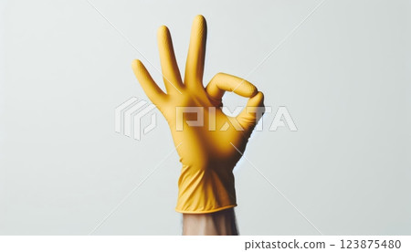 Hand wearing yellow rubber glove showing OK gesture on light background. Household cleaning and hygiene concept 123875480