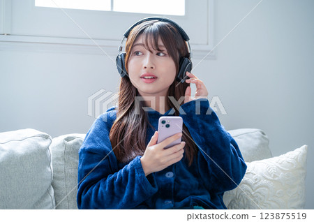 A woman listening to music with headphones and holding a smartphone in the living room in winter 123875519