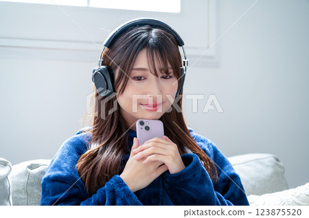 冬天，一位女士在客廳戴著耳機聽音樂，手裡拿著智慧型手機 123875520
