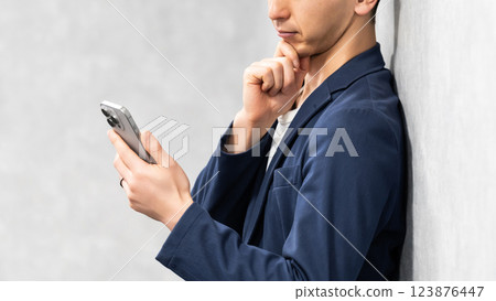 男商人一邊看著智慧型手機一邊思考 123876447
