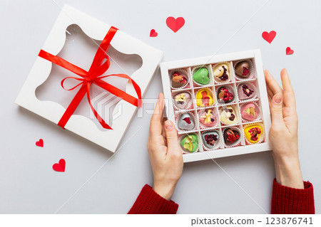 Female hands with delicious candies in box on color background 123876741
