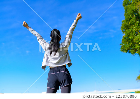 A cool woman with a cool back view posing for the blue sky while walking, stretching, aerobic exercise 123876896